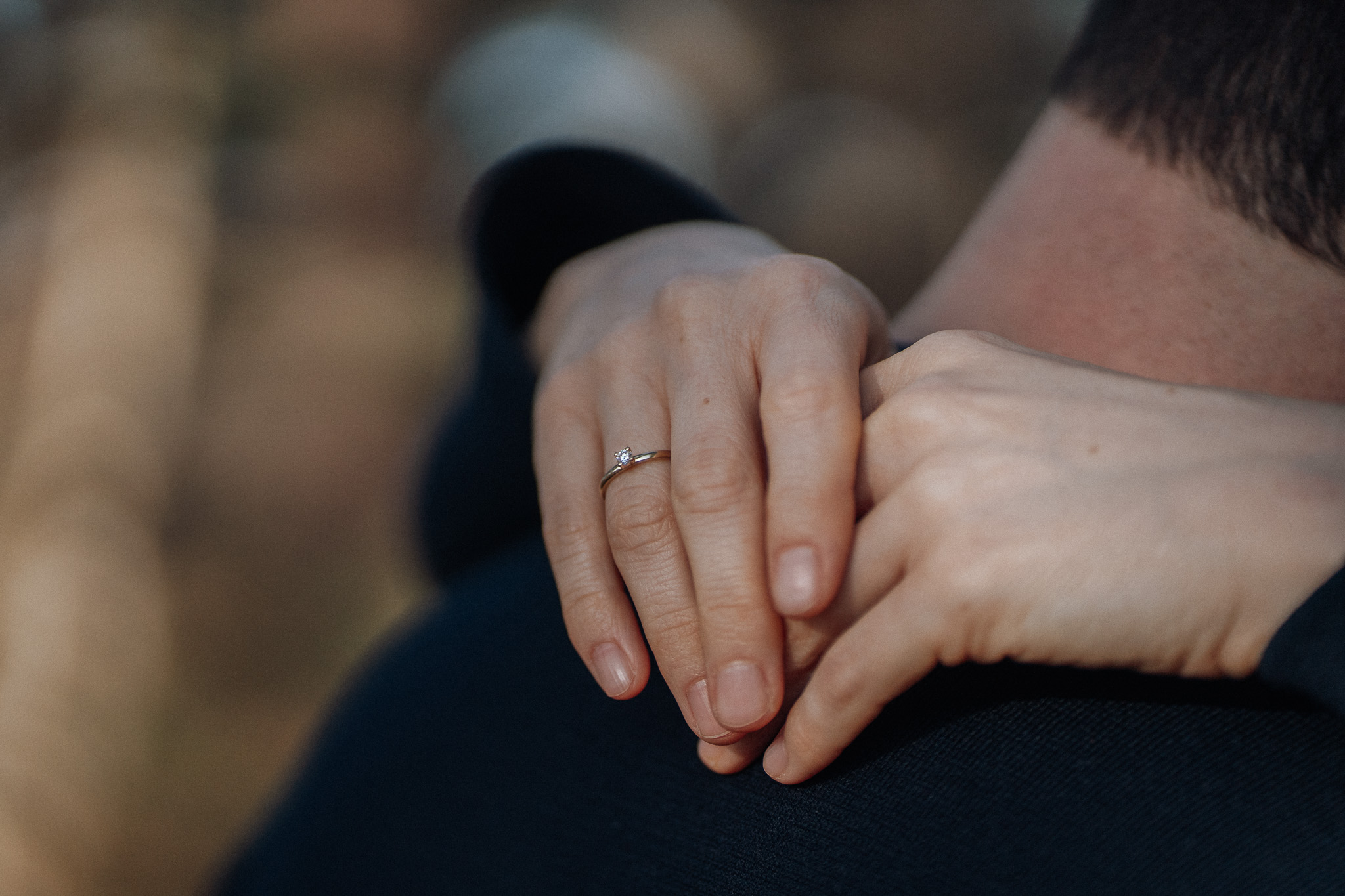 Frau hält den Mann umarmend am Arm, an dem ein Ehering zu sehen ist.